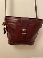 Front view of burgundy leather LUIGI bag with shoulder strap and flap closure featuring gold-tone buckle.