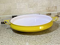 Full view of the yellow enamel cast iron baker/paella pan on counter showing exterior, interior, and side handles.
