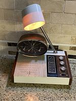 Full view of vintage Mid-Century Modern Longines Symphonette radio clock lamp combination showing wood grain sides, ribbed front panel, oval clock face, and built-in lamp switched on.