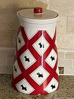 Side view of the vintage ceramic cookie jar showing the red and white lattice pattern with black dog silhouettes and a red knob lid on top.