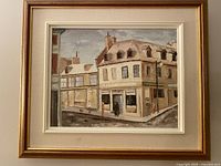 Front view of the framed oil painting depicting a street corner in old Montreal with beige buildings and cloudy sky.