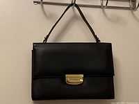 Front view of the black leather handbag showing folded flap and gold-tone clasp.