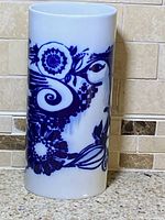 Tall cylindrical white porcelain vase with blue abstract owl and floral design shown from front angle