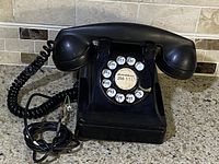 Front view of the vintage black rotary dial telephone with handset on top and cord wrapped.