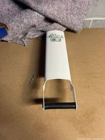 Front view of white manual aluminum can crusher showing Chateau branding and black handle, placed on cardboard with wall and blanket background.