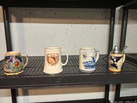 Four vintage beer mugs and cups displayed on a metal shelf against concrete wall