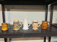 Five beer mugs on a black metal shelf, displaying varied ceramic styles and colors