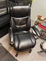 Front view of the black swivel office chair showing cushioned seat, backrest and padded armrests.