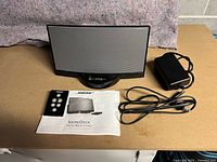 Full lot showing Bose SoundDock speaker dock, remote control, power adapter, and user manual on a brown surface.