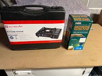 Full lot view showing Outbound propane stove carrying case and box packaging for the drinking water pump.
