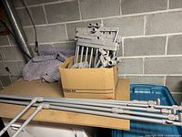 Cardboard box containing multiple gray plastic poles, connectors, and joint pieces for closet organizer.