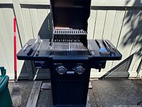 Front view of the Coleman Revolution gas grill, showing grill surface, burner controls, side shelves with tools and rotisserie.