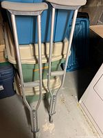 Full view of the pair of silver aluminum crutches with gray padded hand grips and underarm supports, standing upright against a background.