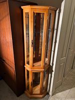 Full view of the tall wood curio cabinet showing its glass paneled doors and wood base.
