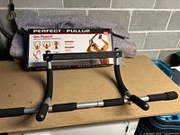 Full view of Perfect Pullup doorway exercise bar on tabletop with packaging behind it.