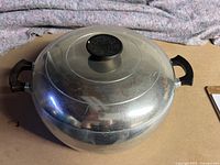 Closed view of the vintage aluminum Dutch oven showing the dome-shaped lid with a black knob handle and two black side handles.