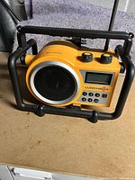 Front angle of yellow Electrohome Lunchbox radio in black protective frame, showing speaker and control knobs on top.