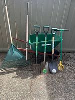 Full set of gardening tools and wheelbarrow against grey fence on gravel ground