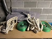 Two green heavy duty lifting slings and two coiled synthetic tow straps on a flat surface with a gray blanket in the background.
