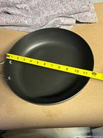 Top view of the black non-stick frying pan with yellow measuring tape showing approximately 12 inches diameter.