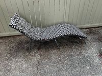 Black and white geometric patterned cushion resting on a similar lounge chair frame, displayed outside.
