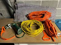 Three outdoor extension cords (two orange, one yellow) coiled on table with green outdoor timer lying next to them.