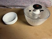 Side view of six stacked white CorningWare soup bowls with Oxo salad spinner to the right.