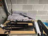 Multiple black metal light stands with clamps laid out on table with cloth underneath.