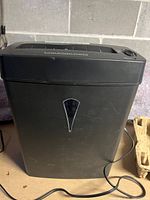 Front view of the black Royal paper shredder unit with power cord visible and triangular window for wastebasket level.