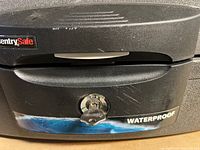 Close-up of the SentrySafe waterproof safe front showing key lock with key inserted, SentrySafe logo, and waterproof label.