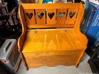 Front view of wooden storage bench, showing heart cutout backrest and hinged seat.