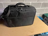 Black laptop bag with zippers, handles, shoulder strap on wood surface