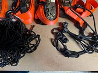Close up photo showing four orange ratchet tie down straps with metal ratchets and black hooks plus coiled black elastic cargo nets with hooks.