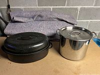 Photo showing black speckled metal turkey roaster and stainless steel stock pot side by side on surface.