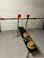 Weight bench with barbell and red collars, weights on bench.