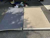 Two carpets laid out side by side on pavement showing beige and gray colors and size comparison.