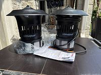 Two black Dynatrap mosquito traps DT110-CA placed side by side on a table, showing overall size and shape, includes power cords and packaging.