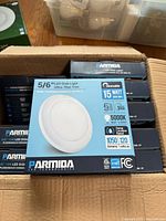 Box of ten Parmida 5/6" LED Disk Lights with ultra thin trim stacked in cardboard box, packaging shows specifications including 15 watt equivalent power, dimmable, 1050 lumens, 5000K daylight color, and damp location rating.