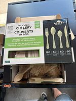 Photo of a box of Forest For Climate wooden cutlery, showing packaging and some utensils partially exposed.