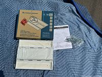 Photo showing the Lithonia Lighting CPHB Linear LED Highbay light, its original box, mounting hardware in orange bag, instruction manual, and metal chain on a blue blanket.