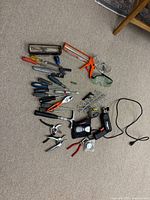 Full view of assorted hand tools, clamps, safety goggles, caulking gun, and power tool cords on carpet