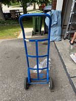 Front view of blue metal dolly showing metal frame, black wheels, and rusted metal base plate.
