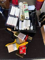 Paint brushes and roller frame along with some loose roller covers spread on a table.