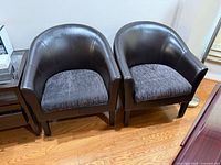 Front view of the two dark brown leatherette barrel chairs with brown patterned cushions, showing style and condition.