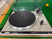 Technics turntable front view with clear dust cover raised, showing platter and tonearm