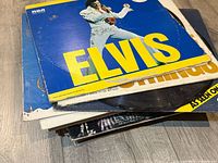 Stack of vinyl LP records featuring Elvis Presley prominently on top with other records beneath showing wear and some visible artists