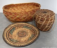 Three woven baskets arranged: a large oval reddish American basket, a flat round patterned American basket, and a rounded brown African basket with handle.