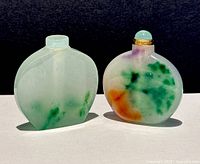 Two natural jade Asian perfume and snuff bottles; one pale green translucent with smooth finish, other rounded flat form with multicolor swirls and green rounded stopper with gold-tone collar