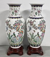 Front view of the pair of ceramic Asian vases showing detailed floral and bird designs with attached wooden bases.