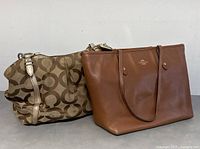 Two Coach bags shown together: One brown leather tote and one brown signature fabric handbag